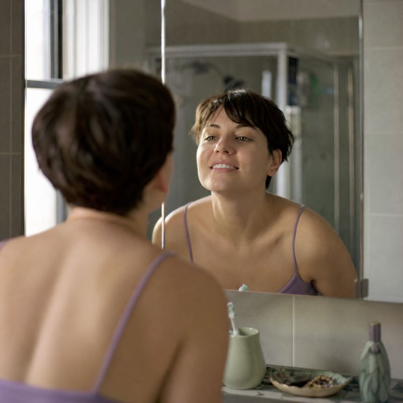 A woman checking her front teeth in a bathroom mirror